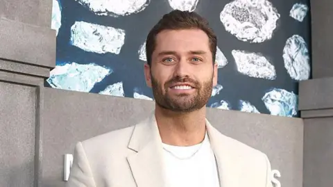 Getty Images Reality star Dakota Mortensen of The Secret Lives of Mormon Wives attends a premiere for the Hulu series in a white shirt and cream coat.