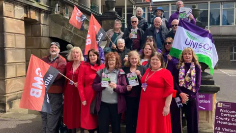 Labour councillors and union campaigners gather on the steps of Matlock County Hall waving flags in a rally in support of the care homes and day centres under threat