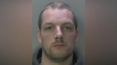 A police mugshot of Dion Arnold, a man with short brown hair in a grey hoodie.