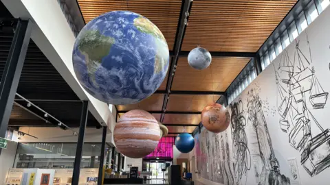 Luke Deal/BBC A view of a ceiling where inflatable planets have been hung up.