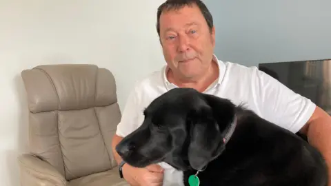 A man with a black labrador in a living room