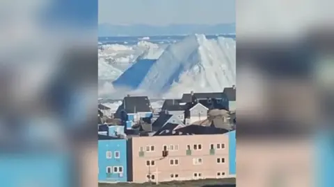 Massive iceberg towers over a small coastal town