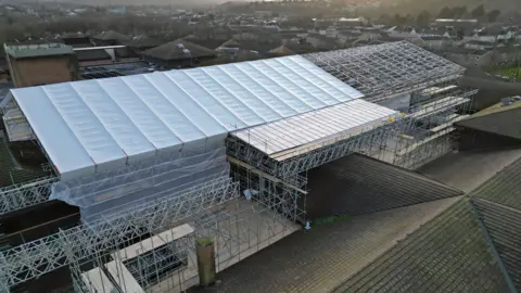 The aerial picture shows a large section of the roof under scaffolding and a canopy. The old roof which is yet to be replaced is also visible on a separate part of the building.