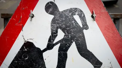 A large triangular roadworks sign with a red border