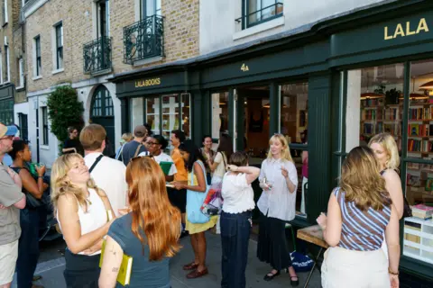 People standing outside a shop with green awning and the lettering 'Lala Books'