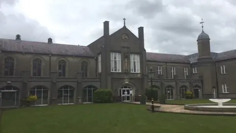 BBC The St David's Building, known as the old building, at the Lampeter Campus. It is grey with a lawn, path and water feature, in front of it