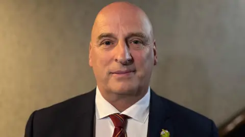 A man wearing a dark blazer and white shirt with red tie