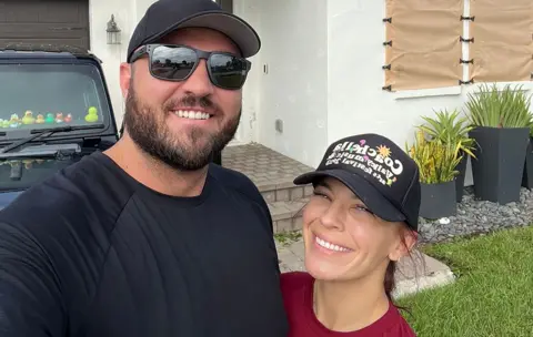 Chynna Perkins Sterling and Chynna Perkins, both wearing black hats, stand in front of a house