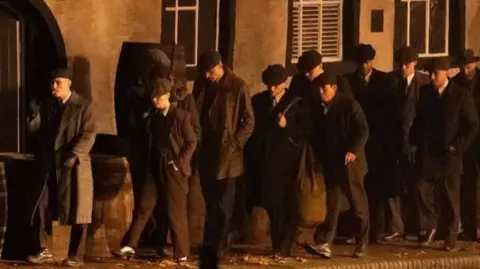 Spencer Elcock A group of men in 1940s clothing walking along the side of a canal