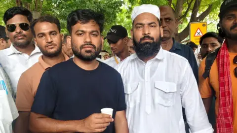 Mohammad Junaid CJP founder Abhijeet Dipke in a black shirt and holding a paper glass poses with Junaid, who's wearing a white tunic and a skull cap.