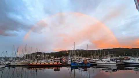 Donald and Caitlin Wilkins Rainbow sunset above boats on a loch