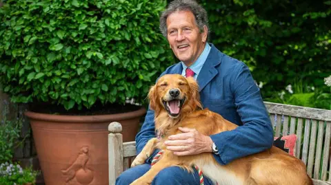 Getty Images Monty Don, a middle-aged man in a blue suit, has an informal moment with his golden retriever Ned