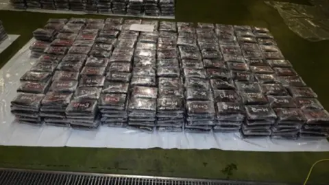 NCA A huge pile of black wraps of cocaine laid out on the floor.