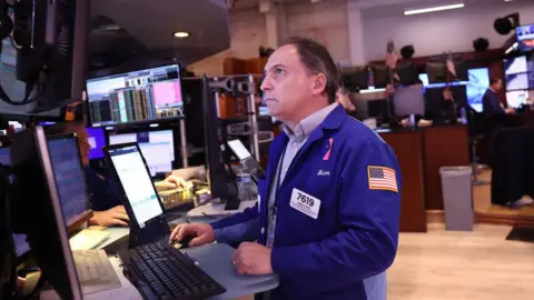 Getty Images A trade on the New York Stock Exchange anxiously looks at screen with share prices