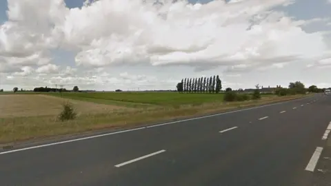 Part of the A47 between Thorney and Eye in Cambridgeshire. The surrounding landscape is flat and there are fields and trees in the background