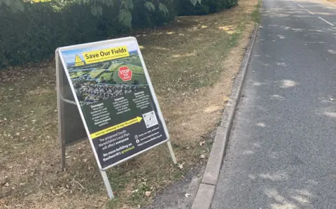 A Save our Fields poster is on an A3 size board at the side of the road on Rouncil Lane in Kenilworth