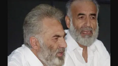 PA Media Two men with grey hair and beards, both wearing open-necked white shirts, speak into microphones at a press conference.