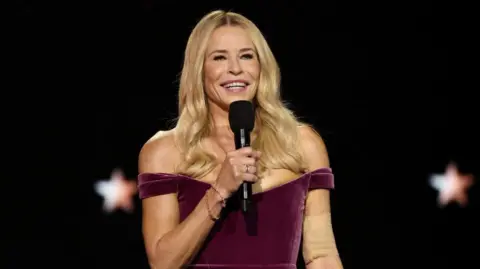 Reuters Chelsea Handler smiles as she addresses the audience on stage at the Critics Choice Awards. She is holding a black microphone up to her mouth and is wearing a purple dress