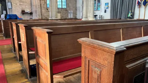 Tom Jackson/BBC Wooden pews with red seat pads. The church pillars can be seen in distance.