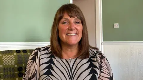 Karen Ashby, lead social prescriber for Nuneaton and Bedworth Primary Care Network sat on a green patterned sofa with a moss green wall behind her.