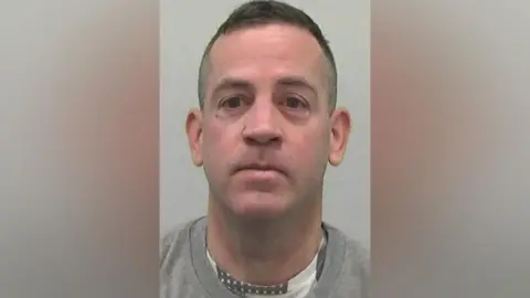 Mugshot of Hodgson. He is clean shaven with a long thin head and short dark hair.