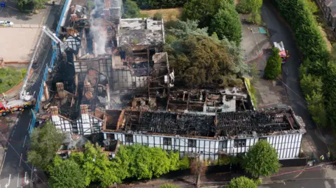 Jacob King/PA Wire An aerial view of the site from last summer, showing smoke billowing into the air and sections of the roof with holes in it. 