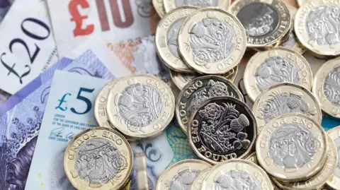 Pound coins piled on top of bank notes including £5, £10 and £20.