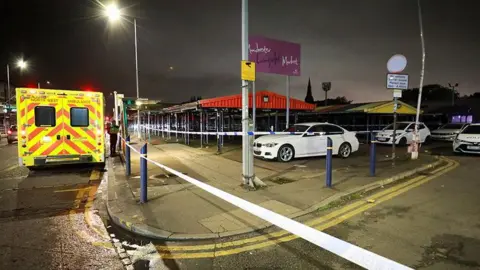 Area by Longsight Market cordoned off by police tape with ambulance and police vehicles there