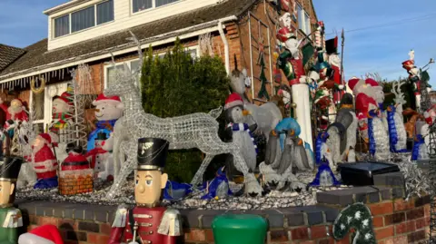 John Devine/BBC It is daytime. Part of the house is covered in lights and Christmas decorations. There are snowmen models as well as soldiers, Santa Claus models and penguins.