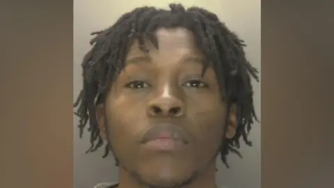 Koketso Ximba - a custody image of a man with black hair in twists