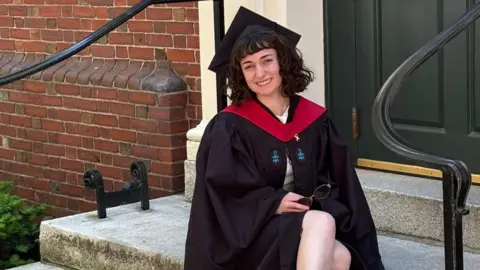 Nitsan Machlis wears a black graduation robe and black hat, pictured smiling