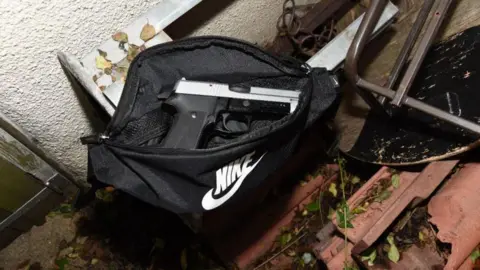 Avon and Somerset Police The 9mm handgun sitting inside an open black Nike bag, which has been hidden behind old furniture and debris in an alleyway. The picture is taken with a flash at night.