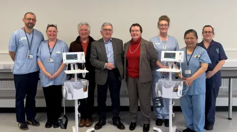 A group of hospital staff and trustees with the two donated monitors in front of them