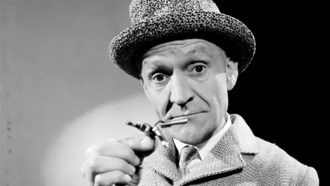 Black and white image of Stanley Unwin in a bowler hat and coat.