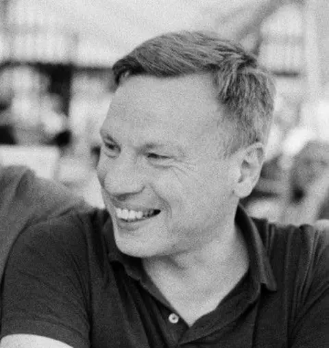 Tristan Copeland A black and white photo of Gary who is laughing and wearing a dark button-up T-shirt.