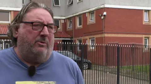 Les Skarratts standing in front of a block of flats called Knowsley Heights