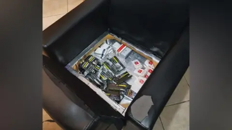 Cigarettes hidden underneath the cushion of a black chair in a specially constructed metal compartment