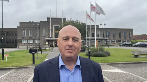 Keith Prince looking into the camera, stood in front of Havering Town Hall