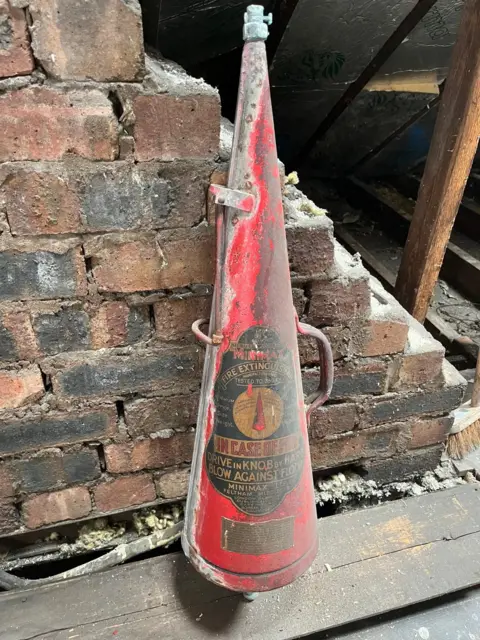 The bottom half of a red fire extinguisher with a black, gold and red label containing written instructions