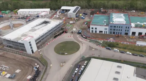 A construction site with a roundabout in the middle and buildings surrounding it.