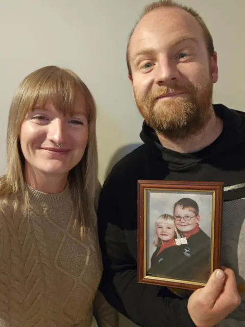 PA Media A woman and a man hold a framed photo of two children.