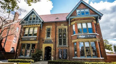 Wells & Co The outside of D'Parys pub, showing a large Edwardian building, with large windows, built from red brick, with two gables.