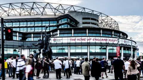 External image of Twickenham stadium, with lots of rugby spectators standing around.