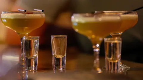 Three cocktails and three full shot glasses on a table