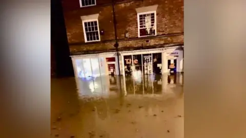 Nicola Eades Dirty flood water swamping a high street with water pictured half way up the front of the windows of two shops