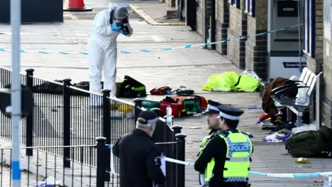 Reuters An area of Huntingdon railway station cordoned off. There are police officer standing outside the cordon. However, a forensics officer stands within the cordon photographing items inside of it.