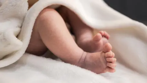 Newborn baby feet on a white sheet with a white blanek over.
