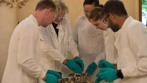 Corpus Christi College, Cambridge Prof John Carr (second left) with Dr Betty Chung (back left) and Robbie Waddell (front right), Jennifer Palmer (second right) and Satish Viswanathan (far right) all in white lab coats and clear safety goggles in Corpus Christi College chapel