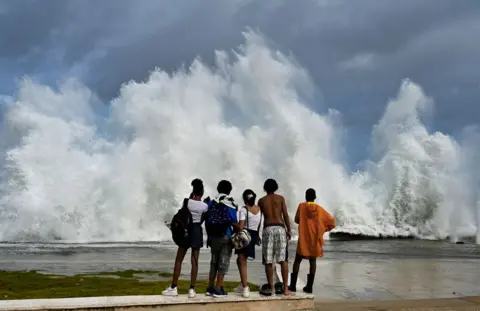 Yamil Lage / AFP  Young people look at waves crashing against the Malecon promenade in Havana due to the passage of Hurricane Milton on October 9, 2024