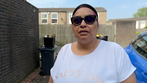 A woman wearing a white t-shirt that says SALTY AIR on it, with black sunglasses and a black do rag